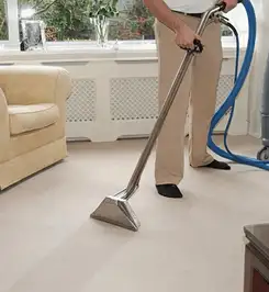 Professional carpet cleaner using a hot-water extraction wand and hose machine in a living room in Baton Rouge, LA.