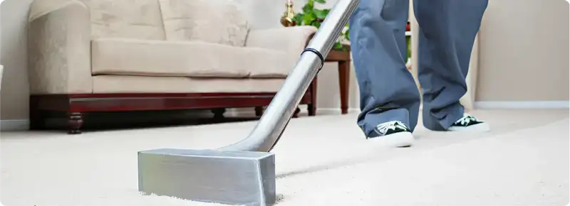 Carpet cleaning technician using a hot-water extraction wand on a light-colored carpet in a living room, Baton Rouge, LA.