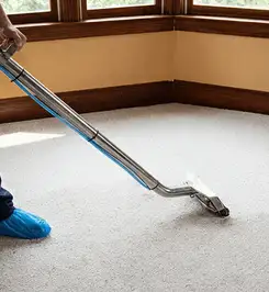 Steam carpet cleaning technician using a hot-water extraction wand on a residential carpet, wearing blue protective shoe covers Baton Rouge, LA.
