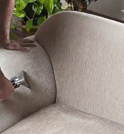 Professional upholstery cleaner deep-cleaning a fabric sofa with a handheld extraction tool and hose Baton Rouge, LA.