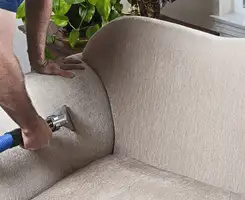 Professional upholstery cleaner deep-cleaning a fabric sofa with a handheld extraction tool and hose in Baton Rouge, LA.